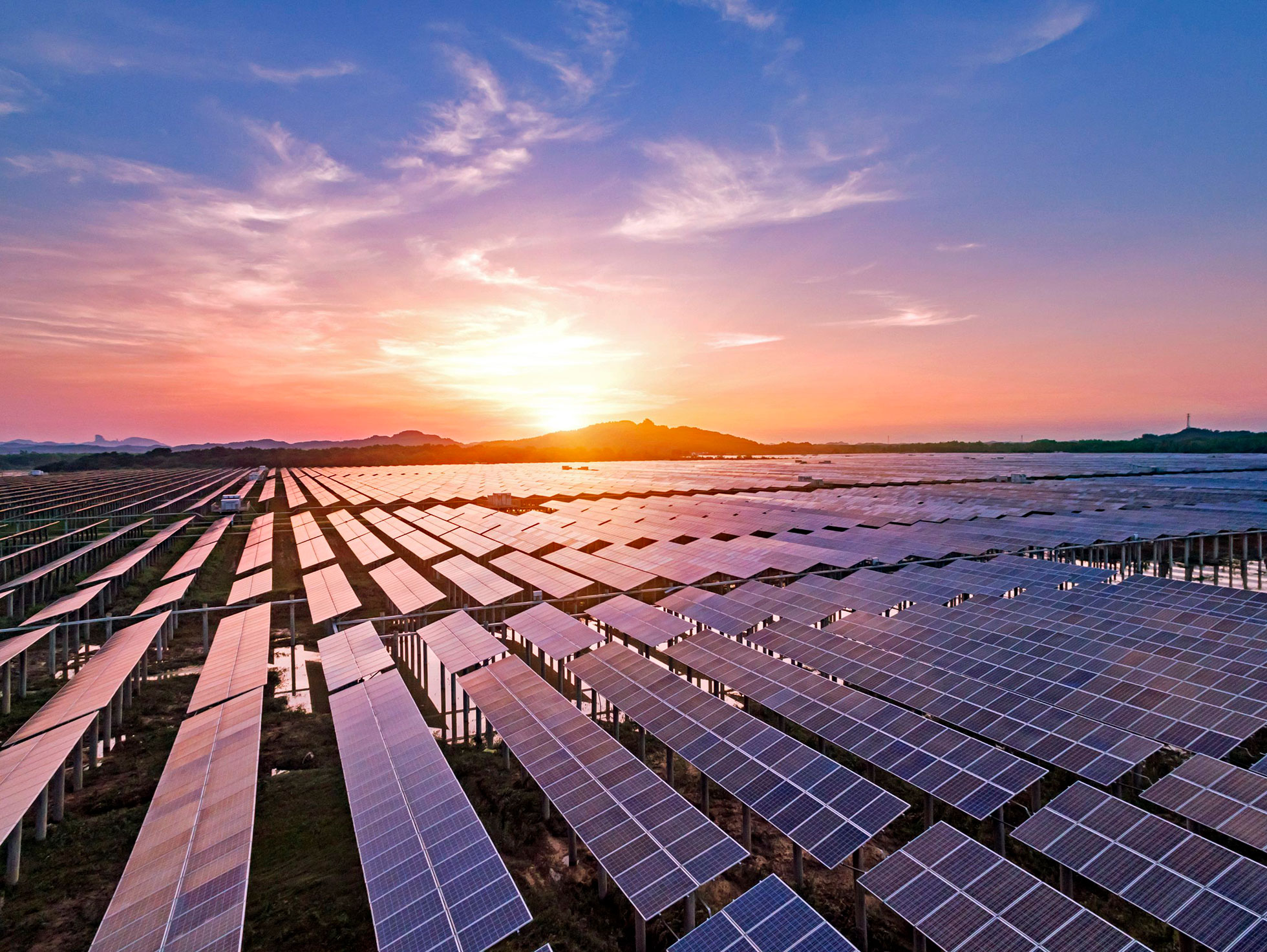 Usina solar de grande porte ao pôr do sol, com fileiras de painéis se estendendo até o horizonte